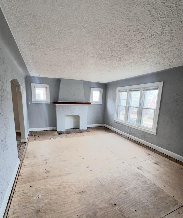 unfurnished living room featuring a fireplace with flush hearth, a textured wall, baseboards, and a textured ceiling