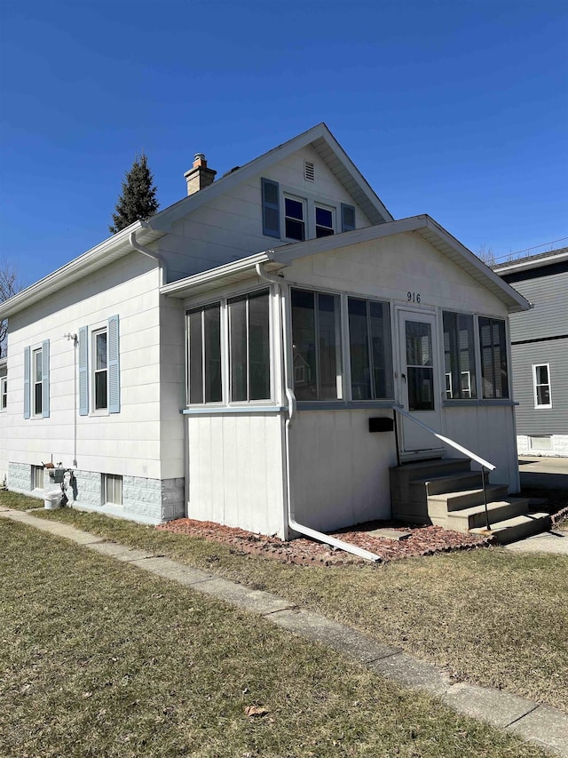 view of front facade featuring entry steps, a chimney, and a sunroom