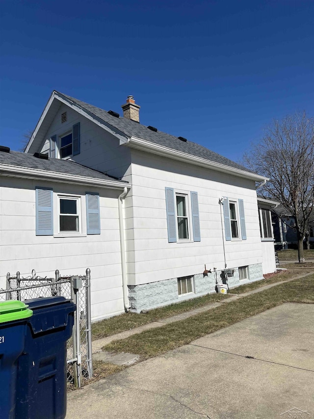 view of property exterior with fence, roof with shingles, and a chimney