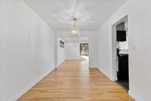 hall featuring a chandelier, baseboards, and light wood-style flooring