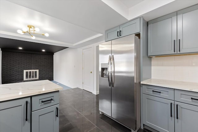 kitchen featuring light stone counters, decorative backsplash, stainless steel fridge, and gray cabinets