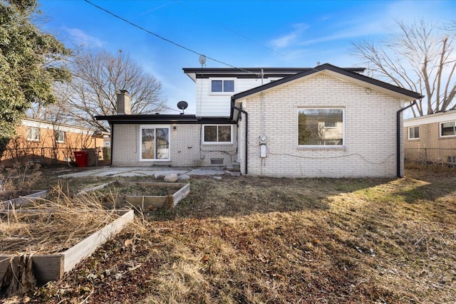 back of property featuring a vegetable garden, fence, brick siding, and a chimney