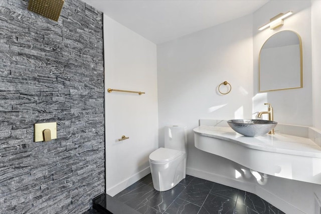 bathroom featuring baseboards, toilet, tiled shower, marble finish floor, and a sink