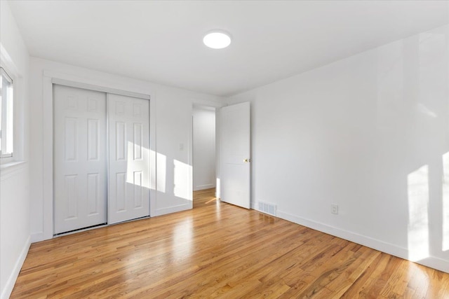 unfurnished bedroom with a closet, visible vents, light wood-style flooring, and baseboards