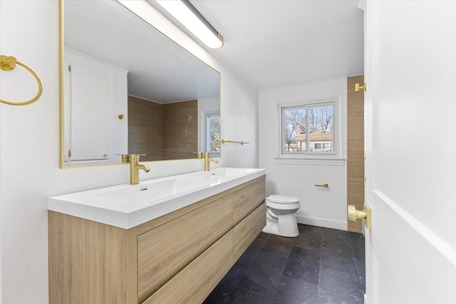 bathroom with double vanity, toilet, baseboards, and a sink