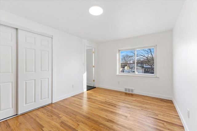 unfurnished bedroom with light wood-style flooring, baseboards, visible vents, and a closet