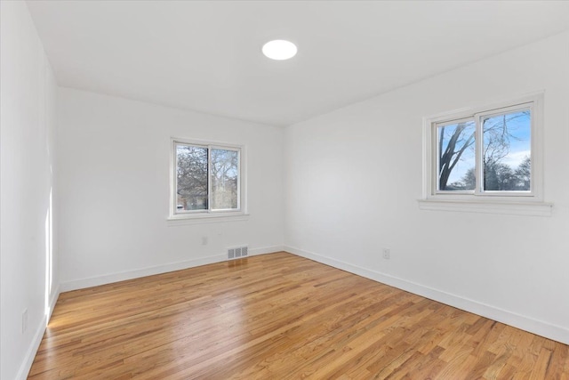 empty room with baseboards, visible vents, and light wood finished floors