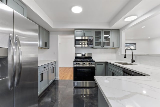 kitchen with light stone countertops, a sink, gray cabinetry, stainless steel appliances, and tasteful backsplash