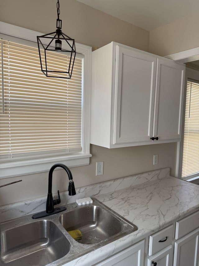 kitchen with decorative light fixtures, white cabinetry, light stone counters, and a sink