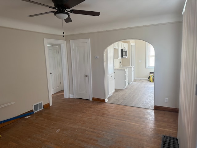 empty room with visible vents, arched walkways, baseboards, and wood finished floors