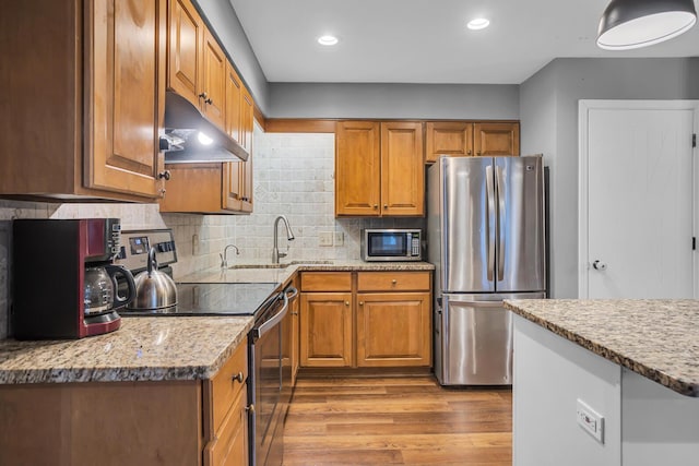 1307 Winston Dr, Jackson, MI 49203 - kitchen with under cabinet range hood, backsplash, wood finished floors, stainless steel appliances, and brown cabinetry