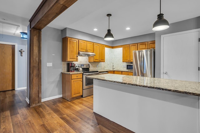 1307 Winston Dr, Jackson, MI 49203 - kitchen featuring light stone counters, wood finished floors, stainless steel appliances, under cabinet range hood, and tasteful backsplash
