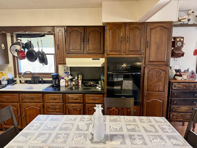 kitchen with under cabinet range hood, black oven, cooktop, and a sink