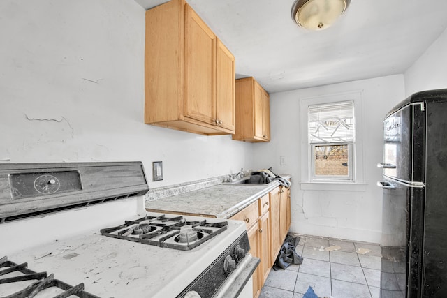 kitchen with white range with gas cooktop, a sink, freestanding refrigerator, light countertops, and light tile patterned floors