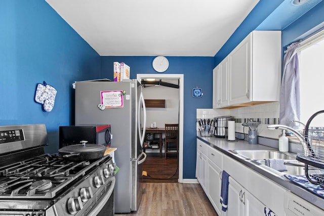 kitchen with stainless steel gas range oven, backsplash, black microwave, light wood-style floors, and white cabinets