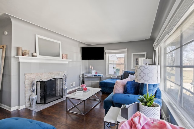 living area featuring a fireplace with flush hearth, visible vents, baseboards, and wood finished floors