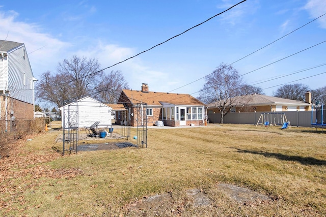 rear view of property with a trampoline, a chimney, a fenced backyard, a yard, and an outdoor structure