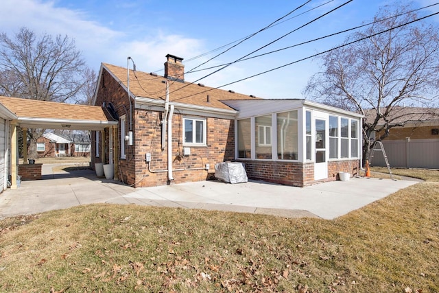 rear view of house featuring brick siding, fence, a lawn, a chimney, and a sunroom