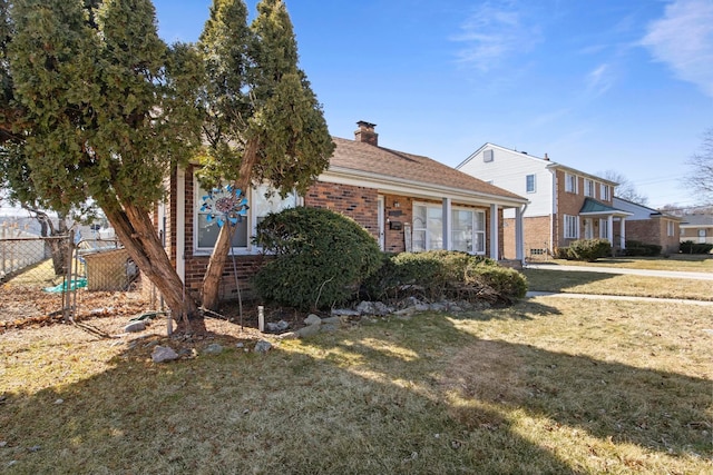 view of front of property with brick siding, a chimney, a front lawn, and fence