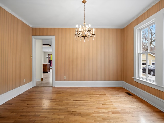 empty room featuring light wood-type flooring, visible vents, an inviting chandelier, crown molding, and baseboards