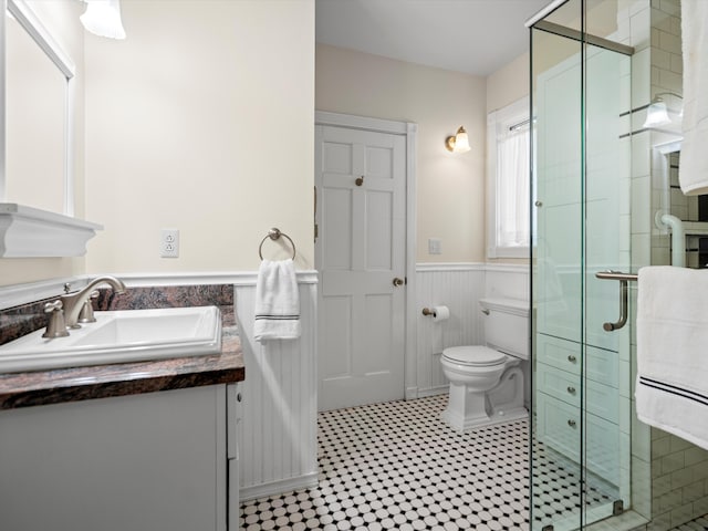 bathroom featuring vanity, toilet, a stall shower, and wainscoting