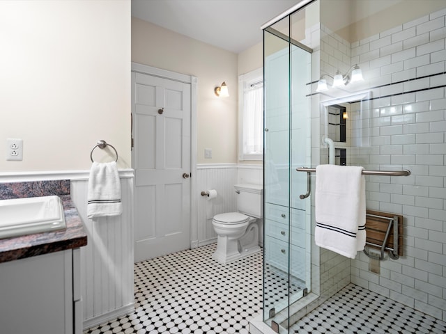 bathroom featuring wainscoting, a stall shower, vanity, and toilet