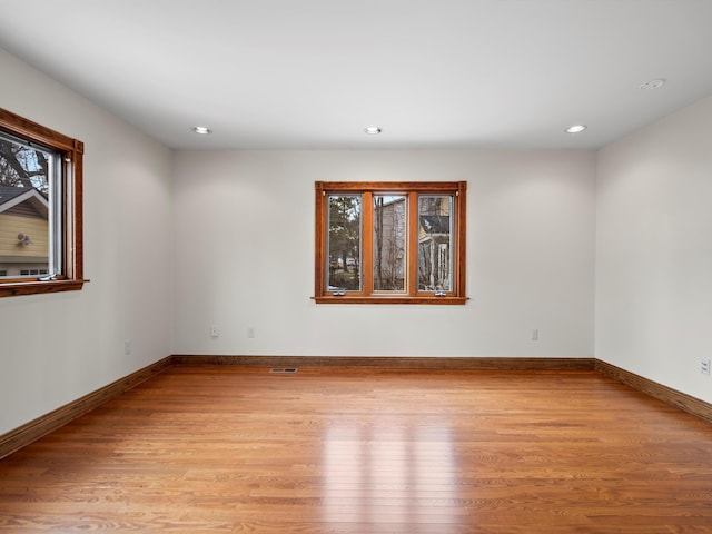 empty room with a healthy amount of sunlight, baseboards, and light wood finished floors