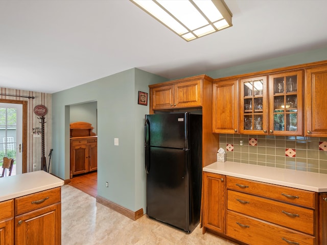 kitchen with decorative backsplash, light countertops, brown cabinetry, and freestanding refrigerator