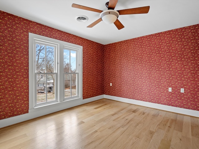 empty room featuring visible vents, light wood finished floors, a healthy amount of sunlight, and wallpapered walls