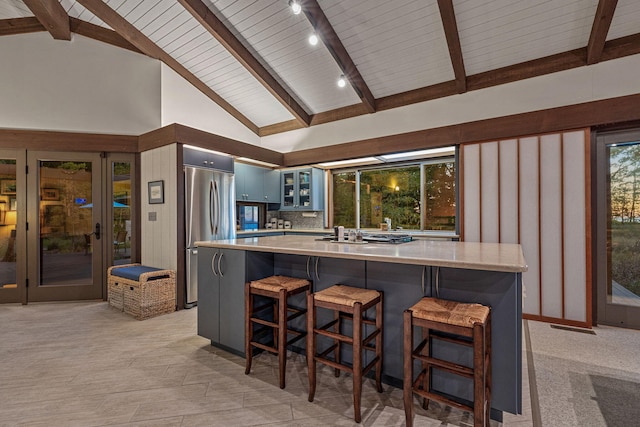 kitchen with beamed ceiling, a breakfast bar, backsplash, stainless steel fridge, and glass insert cabinets