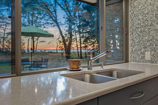 interior details featuring a sink, light stone counters, and gray cabinetry