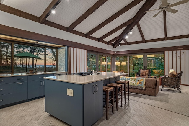 kitchen featuring a kitchen bar, a sink, lofted ceiling with beams, a center island, and light countertops