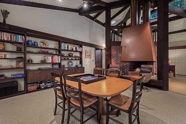 dining room with carpet flooring, beam ceiling, high vaulted ceiling, and a fireplace