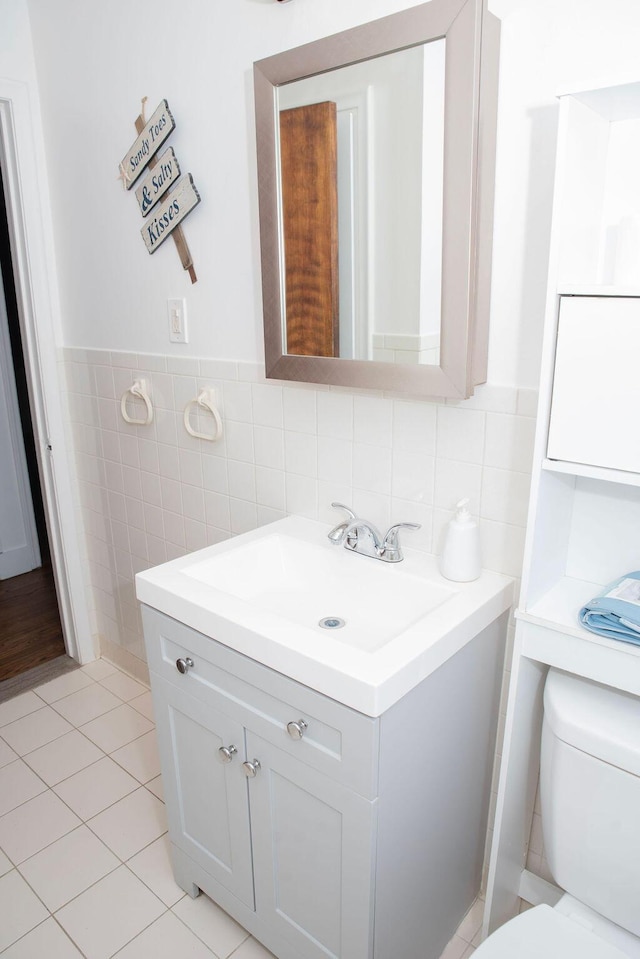 bathroom featuring vanity, a wainscoted wall, tile patterned floors, toilet, and tile walls