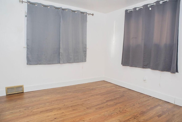 empty room featuring wood finished floors, visible vents, and baseboards