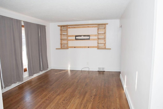 empty room featuring wood finished floors, visible vents, and baseboards