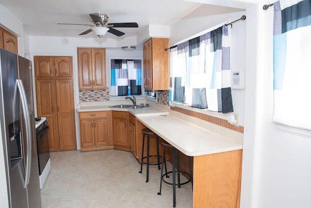 kitchen with stainless steel refrigerator with ice dispenser, a sink, range with gas stovetop, light countertops, and light floors