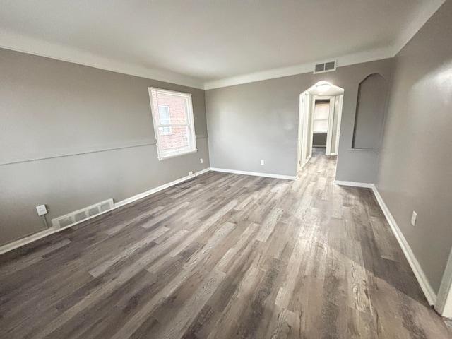 spare room with dark wood finished floors, baseboards, visible vents, and arched walkways