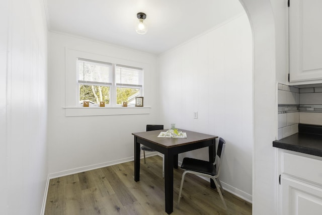 dining area with baseboards, arched walkways, ornamental molding, and light wood finished floors