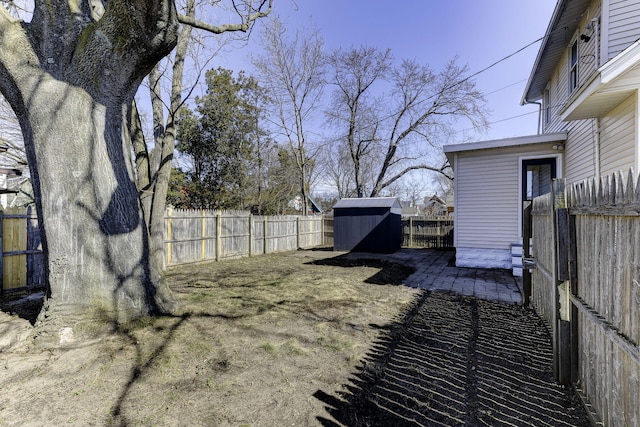 view of yard with a storage unit, an outbuilding, a fenced backyard, and a patio area