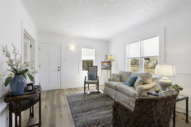 living area with a textured ceiling, light wood-style flooring, and wainscoting