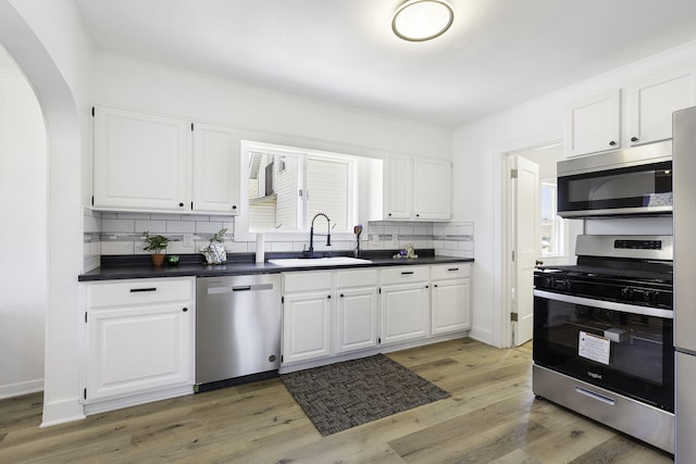 kitchen featuring a sink, decorative backsplash, stainless steel appliances, white cabinets, and dark countertops