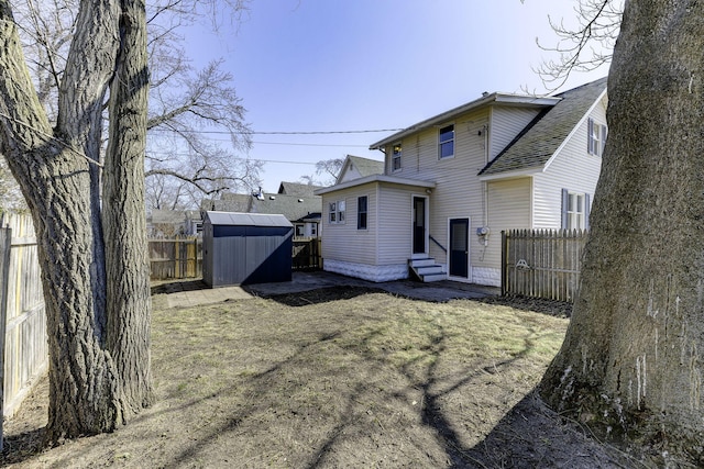 rear view of house with a shed, a fenced backyard, a shingled roof, entry steps, and an outdoor structure