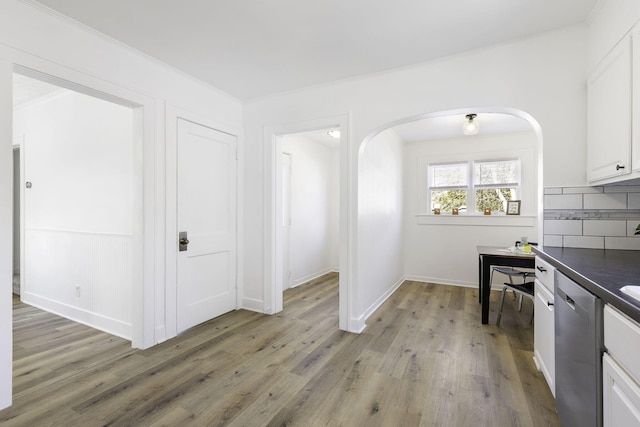 kitchen featuring light wood-style flooring, stainless steel dishwasher, dark countertops, arched walkways, and decorative backsplash