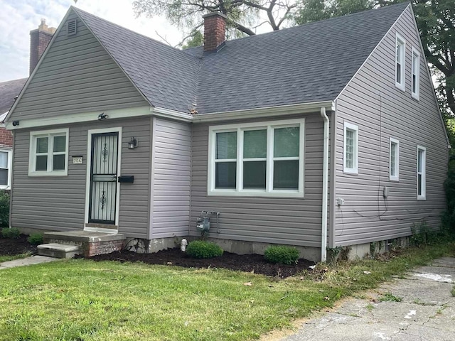 view of front of house featuring a chimney, a front lawn, and roof with shingles