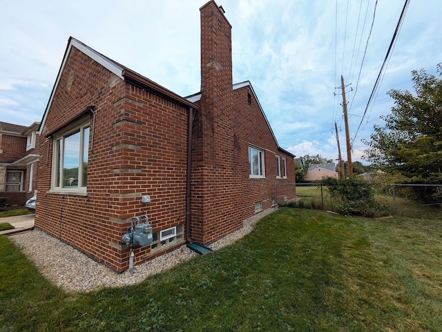 view of side of property featuring fence, a lawn, brick siding, and a chimney