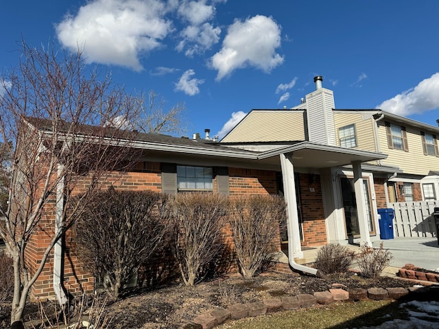 view of home's exterior featuring driveway, brick siding, and a chimney