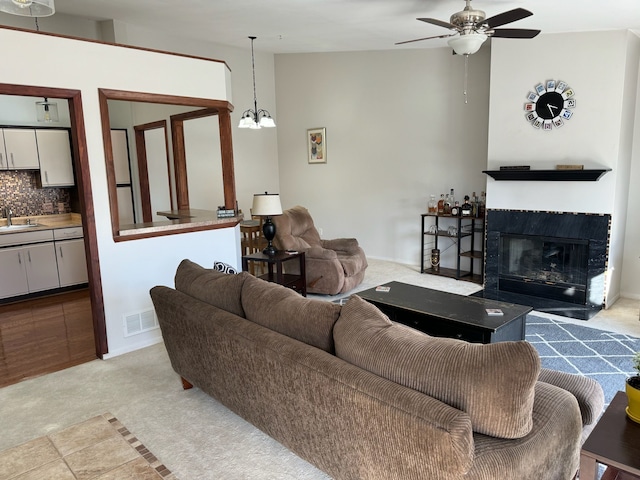 living area with light carpet, visible vents, ceiling fan with notable chandelier, and a tile fireplace