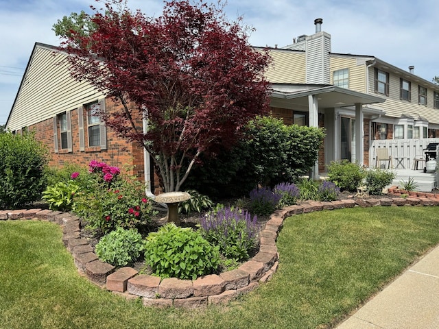 view of side of home featuring a yard, fence, brick siding, and a chimney