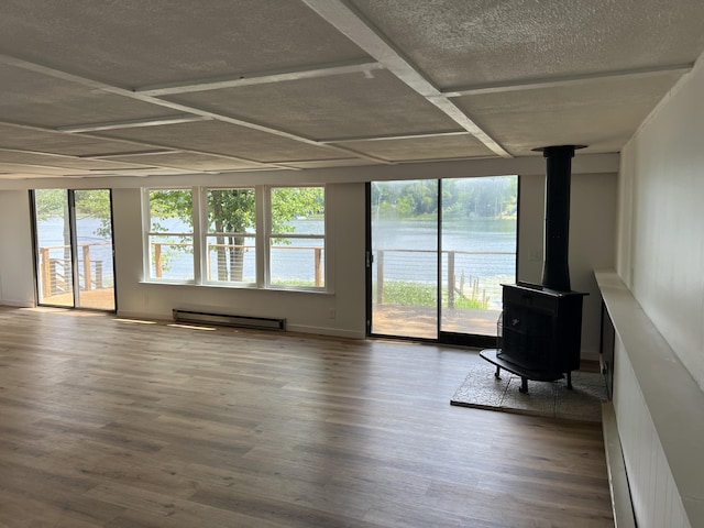 unfurnished living room with wood finished floors, a wood stove, a water view, and a baseboard radiator